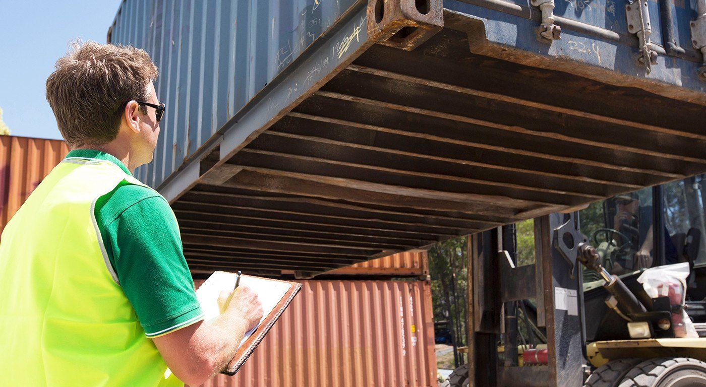 Spencer Ives in a hi-vis vest inspecting the underside of a container lifted by a forklift