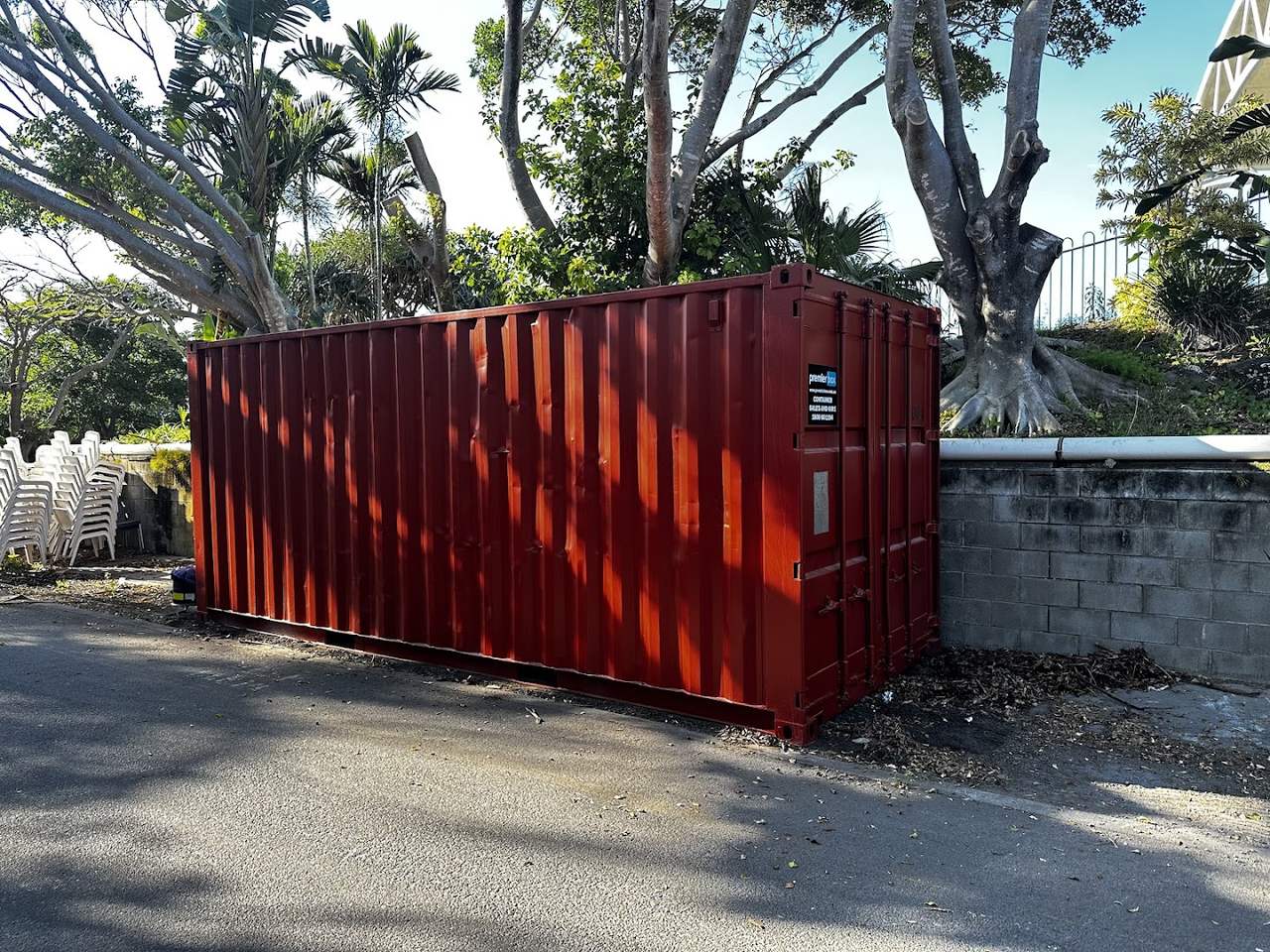 Red 20ft hire container placed on a customer site beside a block wall