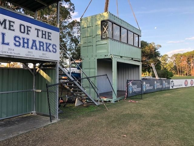 Green stacked shipping container facility with stairs beside an AFL ground