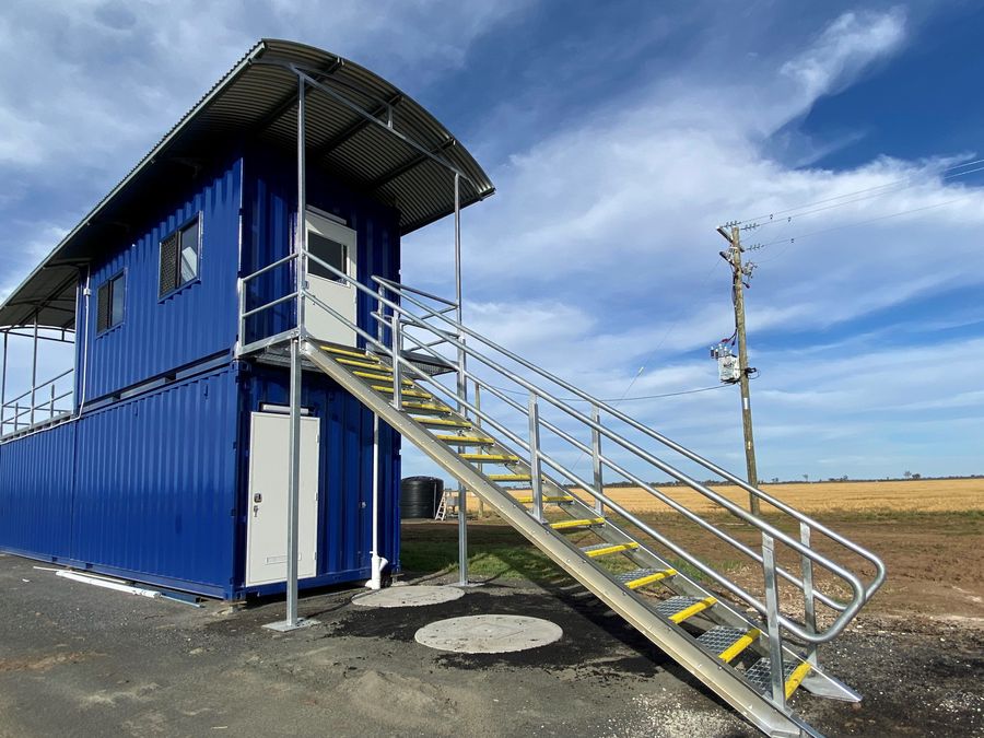 Blue two-storey shipping container facility with an external staircase and curved awning