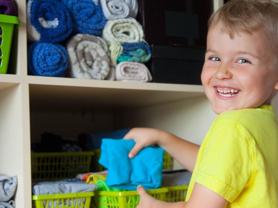 Smiling child putting folded towels onto a storage shelf