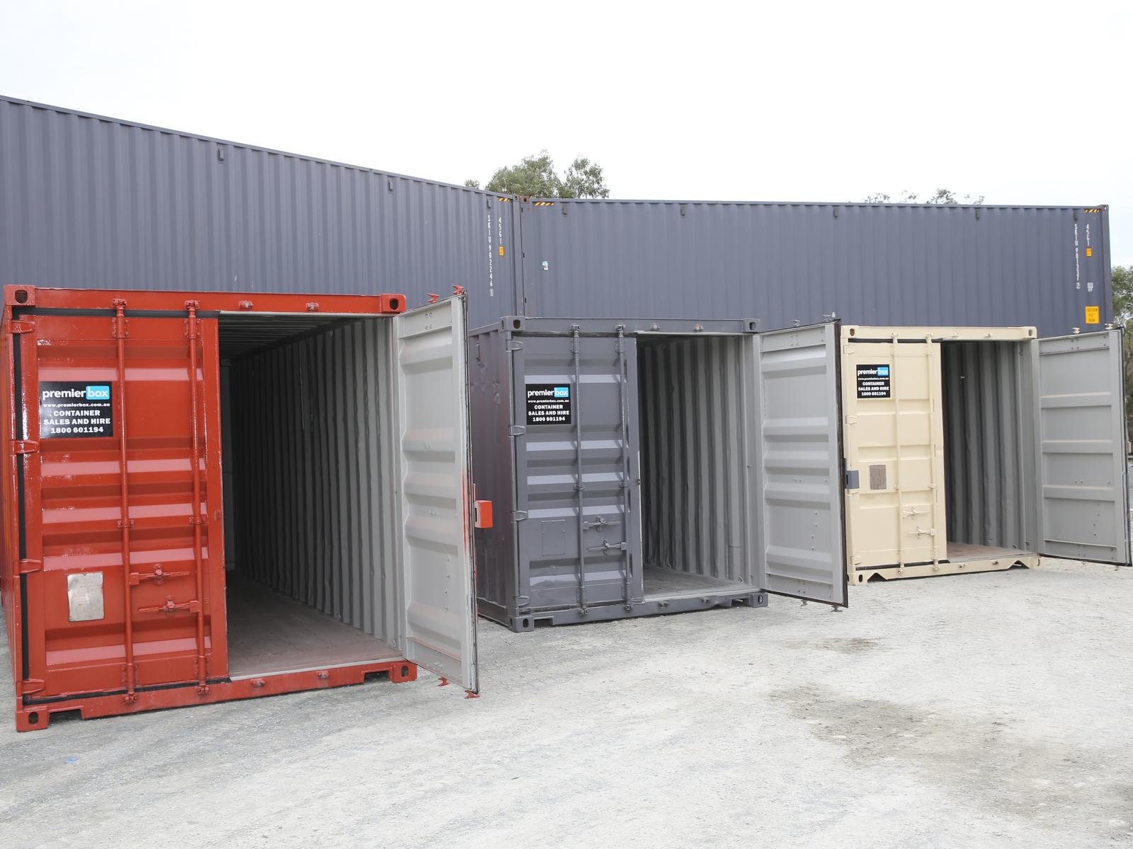 Red, grey and beige used 20ft containers in the yard, the red one with its doors open
