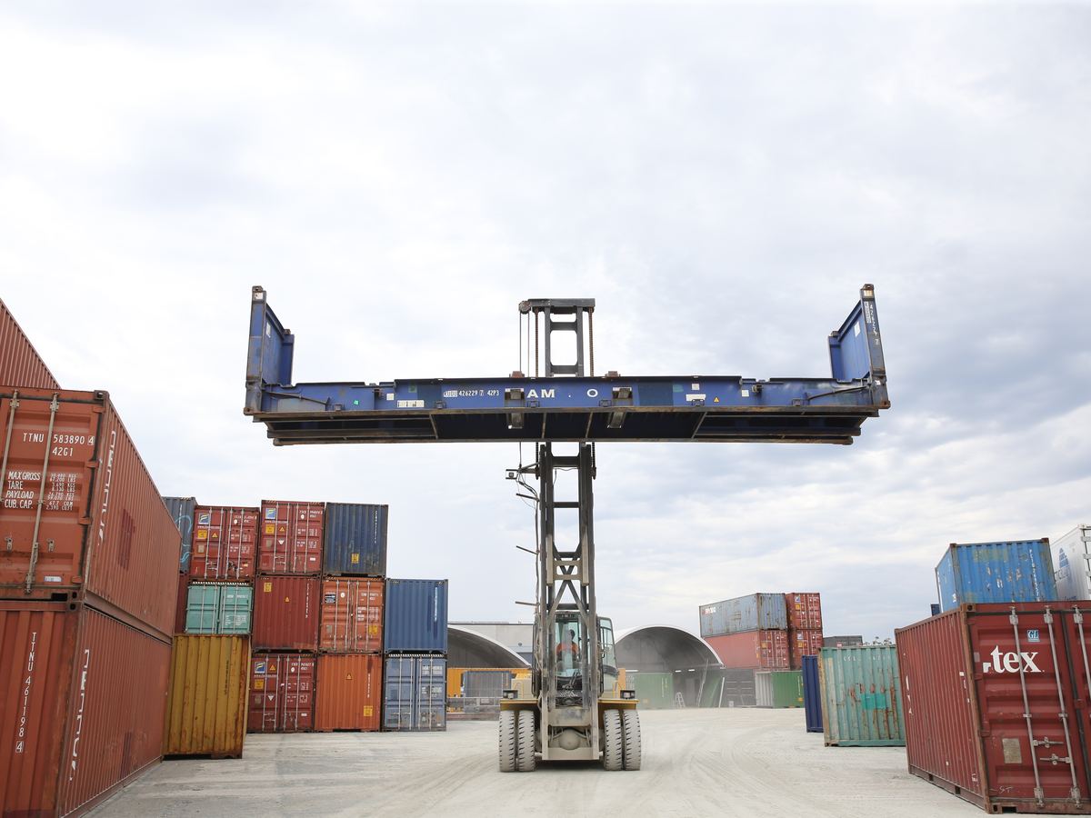 Blue flat rack container lifted by a container handler above the depot stacks