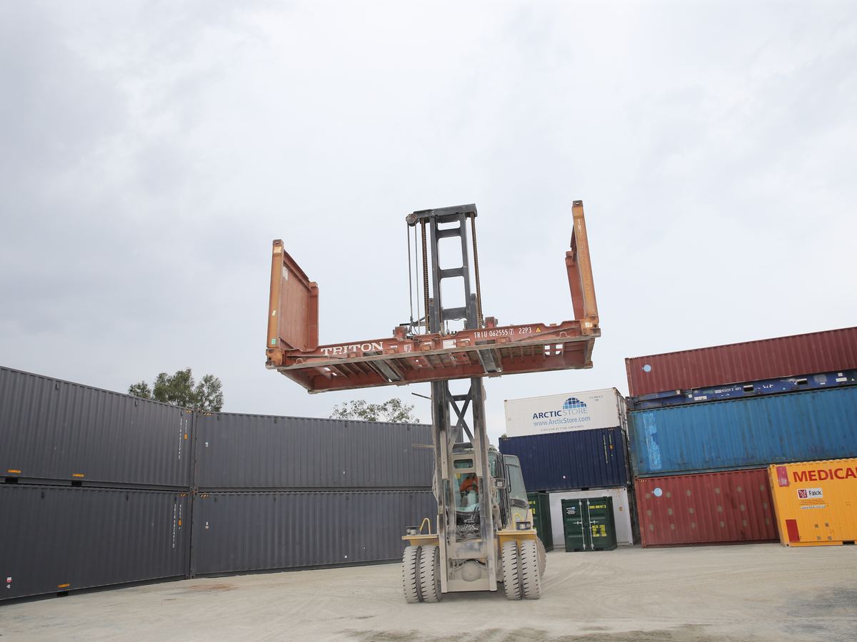 Rust red flat rack container raised by a container handler in the yard