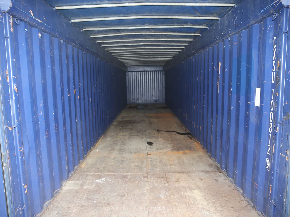 Inside a blue open top container, looking down its length under the roof bows