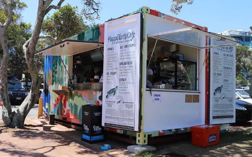Mural-painted Happy Turtle Cafe container kitchen trading under trees, servery windows open