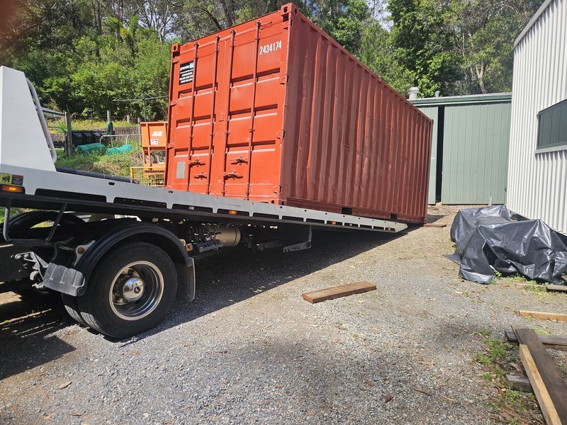 Red shipping container on a tilt tray truck delivered to a customer property