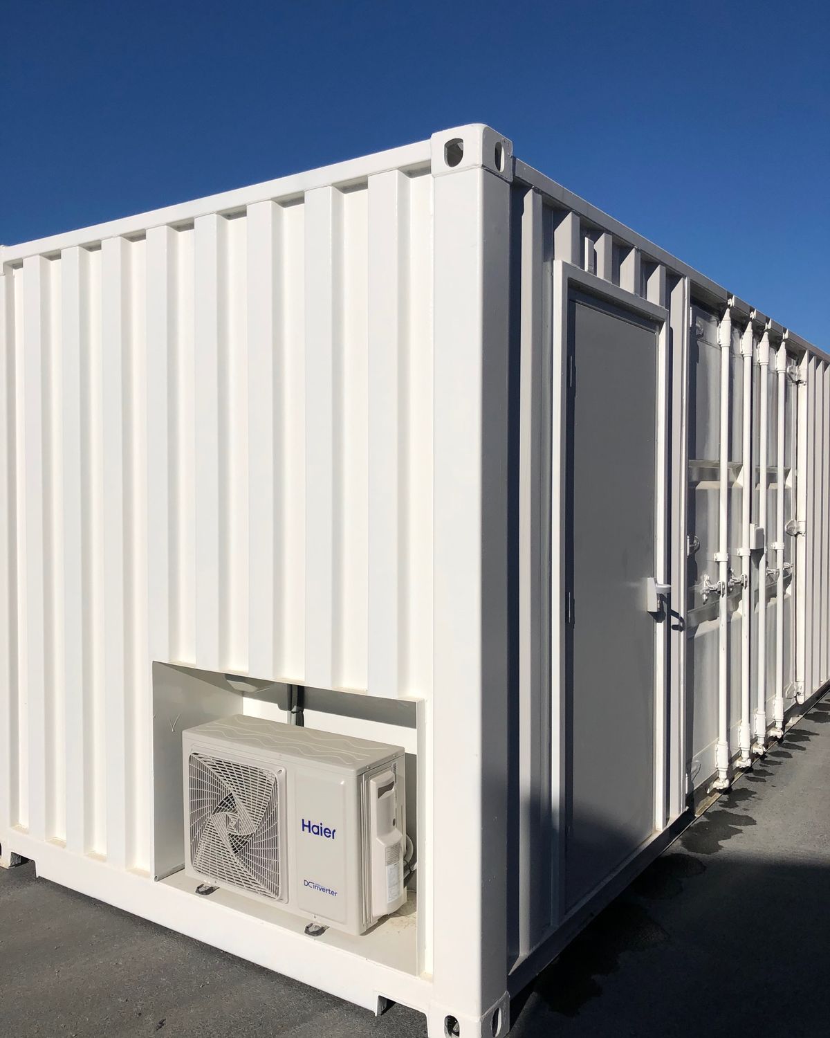 White 20ft shipping container with a wall-mounted air conditioning unit, under a blue sky