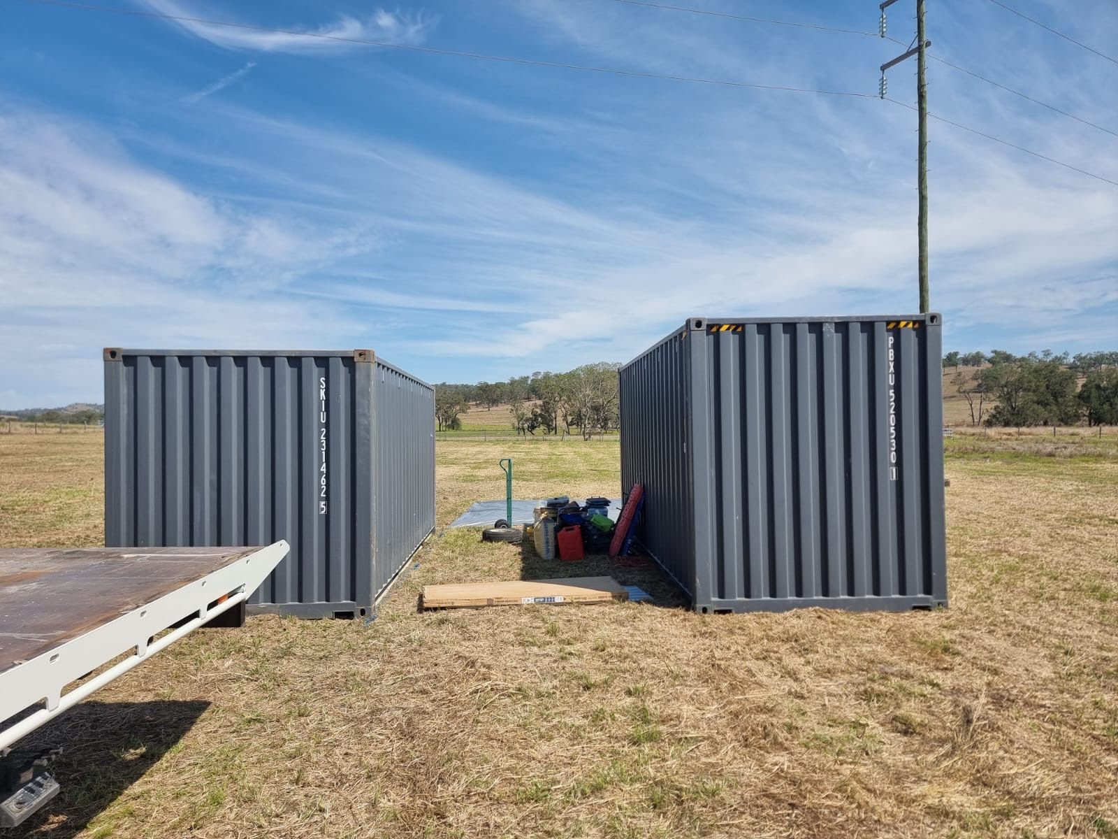 Two charcoal 20ft hire containers placed on a grassy rural site